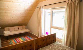 The image shows a cozy bedroom with a double bed and a sofa. Large windows let in plenty of daylight and create a bright atmosphere.