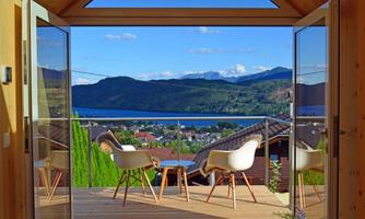 A modern terrace with two chairs and a beautiful view of a landscape with mountains and water. The sky is clear and blue.
