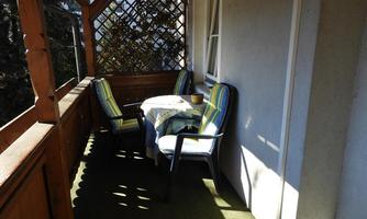 A cozy balcony with two chairs and a table. The furniture is adorned with colorful cushions and there is plenty of daylight.