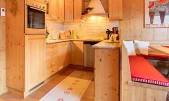 A cozy wooden kitchen with modern appliances and red accents. The dining area is invitingly designed, perfect for friendly meals.
