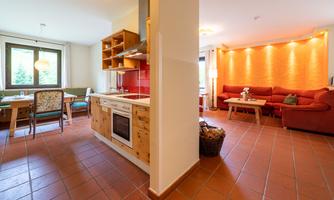 A modern apartment with an open kitchen and dining area. The living space is bright and cozy, featuring a red sofa and warm lighting.
