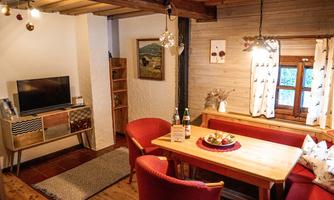 A cozy living and dining room with wooden details. There is a table, red chairs, and a TV corner.