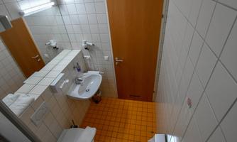 A small, modern bathroom with bright tiles and an orange floor. There is a sink, a toilet, and a wooden cabinet.