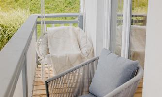 A cozy balcony with a hanging chair and a modern chair. There is a small table with decorative items and candles.