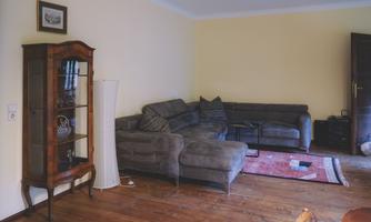 A cozy living room with two gray sofas and a wooden table. There is an antique display cabinet in the room and the floor is made of wood.