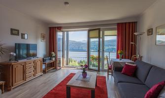 A bright living room with a cozy decor and a view of a lake. Large windows let in plenty of daylight and create a pleasant atmosphere.