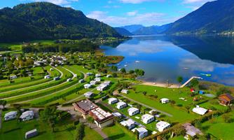 A beautiful campsite by the lake, surrounded by green meadows and mountains. The calm surface of the water reflects the landscape.