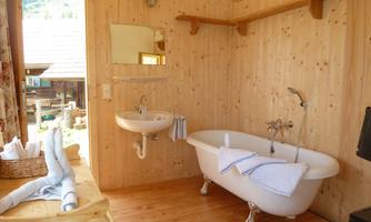 A cozy bathroom with a freestanding bathtub and a sink. The walls are made of light wood, and there are towel-like amenities.