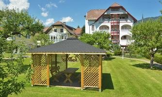 A beautiful pavilion stands in a green garden. In the background, several buildings with wooden and stone architecture can be seen.