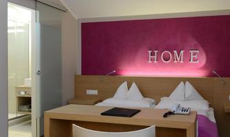 A modern room with two single beds and a stylish pink wall. In the background, a bathroom is visible, separated by a glass door.