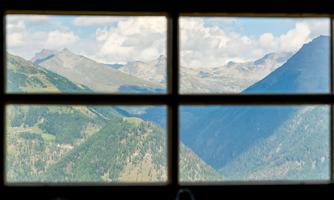 A beautiful mountain landscape with high peaks and green forested slopes. The sky is partly cloudy and offers an impressive view through the window.