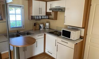 A modern kitchen with wooden cabinets and bright walls. The equipment includes a stove, a microwave, and a sink.