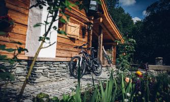 A charming wooden house with a wheel in front of the door. The garden is green and blooming, perfect for a view into nature.