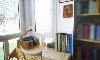 A cozy workspace in a corner with a window. On the table is a record player and books are in a shelf beside it.