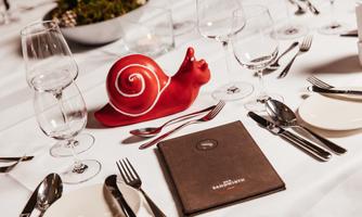 A beautifully set table with glasses and cutlery. In the center is a red snail and the menu card.
