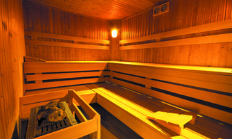 A cozy sauna with wooden-paneled walls and benches. The room is softly lit and feels relaxing.