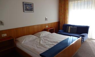 A simple hotel room with a double bed and a couch. Large windows provide plenty of daylight.