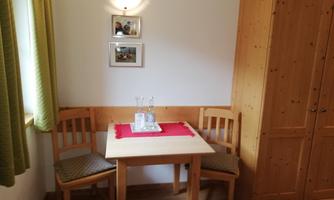 A small dining area with a wooden table and two chairs. On the table, there is a red cloth and a glass carafe.