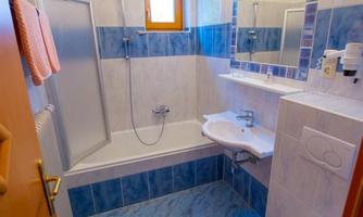 A small, bright bathroom with blue tiles and a window. It contains a bathtub, a sink, and a toilet.