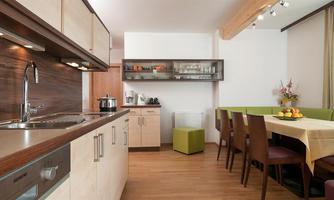 A modern kitchen with wooden shelves and a large dining table. The decor is bright and inviting, with fresh fruits on the table.