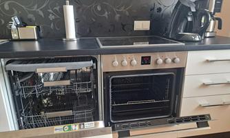 A modern kitchen with a dishwasher and an oven. The countertop is bright and stylish with a black wall design.
