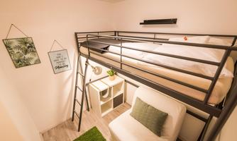 A modern, small room with a loft bed and a cozy seating area. The walls are light, and a plant provides a fresh atmosphere.