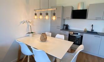 A modern dining room with a white table and four chairs. The kitchenette is bright and well-equipped, with harmonious lighting.