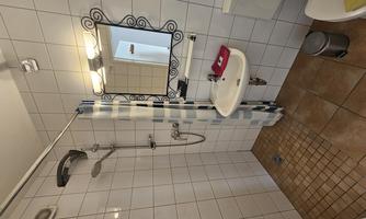 A small bathroom with a shower, sink, and mirror. The walls are tiled and the floor is made of tiles.
