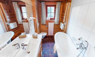 A cozy bathroom with wood paneling and two sinks. The bathtub and window give the room a bright and inviting atmosphere.