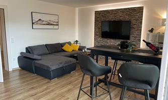 A modern living room with a gray couch and a large television on the wall. The room has a warm wooden floor and an inviting atmosphere.