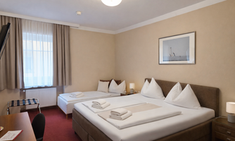 A cozy room with three beds. A large window provides plenty of daylight.