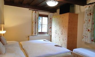 A cozy bedroom with two beds and an additional single bed. There are wooden details and cozy curtains with a floral pattern.