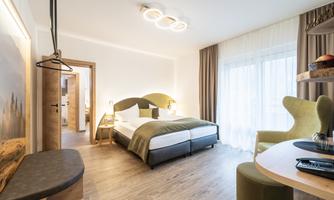 A modern hotel room with a large bed and cozy decor. Large windows provide plenty of daylight.