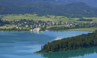 A picturesque lake surrounded by green forests and mountains. The sky is clear and the landscape is peaceful.