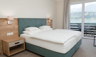 A modern hotel room with a large double bed and a bedside table.  
Large windows offer a view of the landscape.