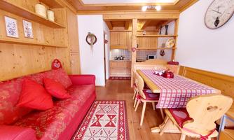 A cozy holiday apartment with wooden walls and a red couch. The dining area is inviting with a table and chairs in traditional style.