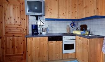 A modern kitchen with wooden furniture and blue accents. It is equipped with a stove, a refrigerator, and a television.