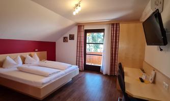 A cozy bedroom with a double bed and two single beds. The room has a desk and a balcony with a view.