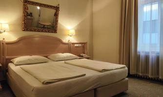 A cozy hotel room with a double bed and a large mirror. The windows are covered with curtains and there is soft lighting from wall lamps.