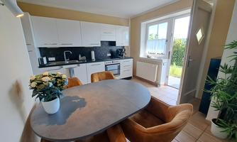 A modern kitchen with white cabinets and a round table. Cozy chairs are at the table, and there is a floral arrangement.