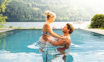 A couple is happily playing in the pool. In the background, a beautiful lake and green landscape can be seen.