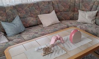 A cozy living room with a large, rounded couch and a wooden table. On the table, there are decorative objects and a tablecloth.