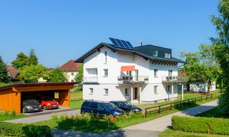A modern house with solar panels and a well-kept garden. In the foreground are several cars and a carport.