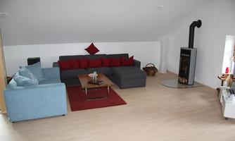 A modern living room with a gray sofa corner and a blue armchair. A wooden table and a fireplace create a cozy atmosphere.