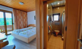 A cozy room with a double bed and wooden paneling. In the background, there is a modern bathroom.