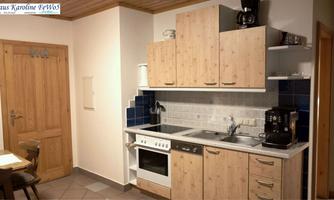 A modern kitchen with light wood cabinets and gray tiles. The equipment includes a stove, a sink, and a coffee maker.