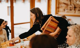 A woman is handing something over to a table with several people. The atmosphere is friendly and sociable.