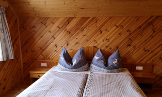 A cozy bedroom with a double bed and wooden paneling. The pillows have a decorative design and the bedding is checkered.