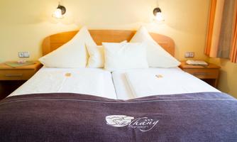 A cozy double bed with white pillows and a dark gray blanket. The room is bright and friendly with orange curtains and bedside lamps.