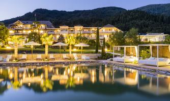 An elegant hotel in the evening, surrounded by mountains. The pool reflects the lights and the soothing ambiance.